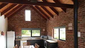 A kitchen with wooden beams, brick walls, a window, and a sink. - Prom Coast Holiday Lodge - Cottage 1 (Waratah North)