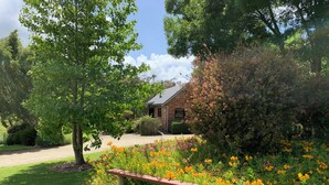 A brick building with a gravel driveway and a grassy lawn. - Prom Coast Holiday Lodge - Cottage 1 (Waratah North)