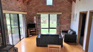 A living room with a fireplace, a sofa, a television, and a dining table with chairs. - Prom Coast Holiday Lodge - Cottage 1 (Waratah North)
