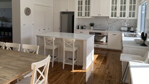 Una cocina moderna con armarios blancos, una isla central con taburetes y un horno empotrado, además de un amplio ventanal que proporciona luz natural.