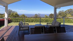 Un espacio al aire libre techado con terraza de madera, dos sillas, una mesa y vistas a un paisaje lejano.