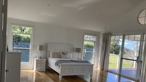 Un dormitorio amplio con una cama grande, dos mesitas de noche y vistas a un paisaje verde a través de amplias ventanas.