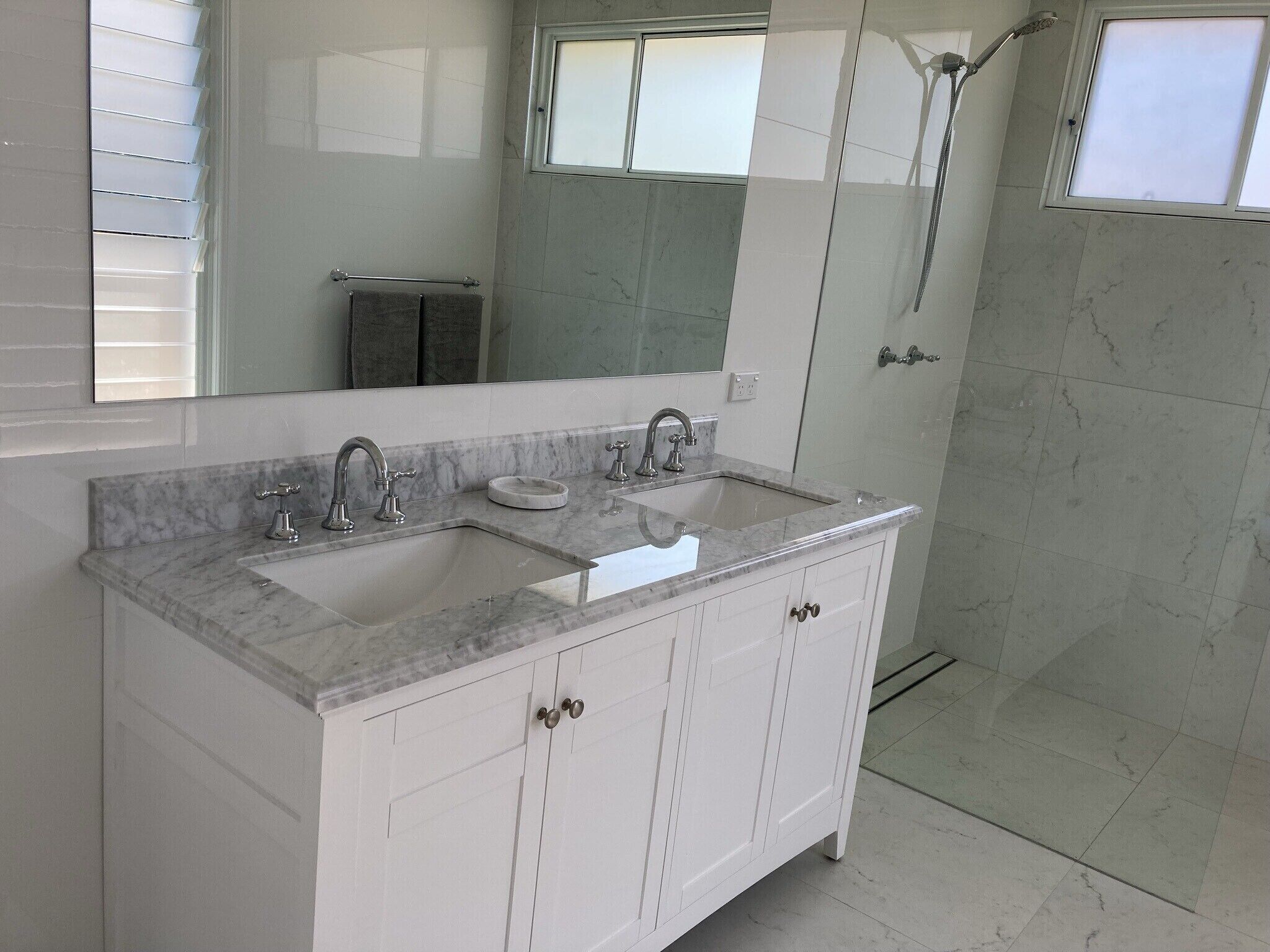 Une salle de bain avec un meuble-lavabo à deux vasques, un grand miroir et un espace douche.