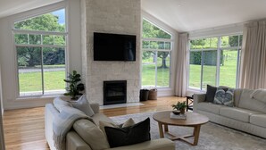 Un salón espacioso con chimenea de piedra, ventanas amplias y un televisor de pantalla plana.