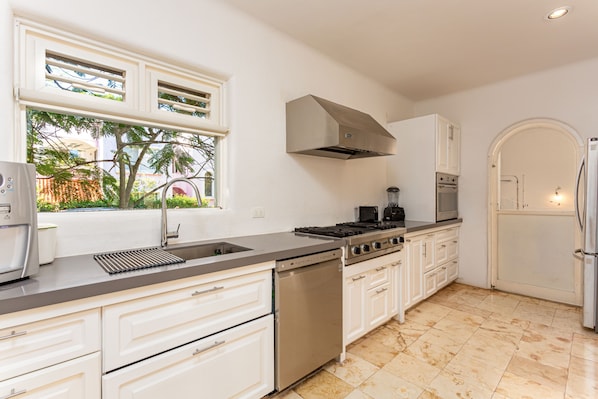 A modern kitchen with white cabinets, stainless steel appliances, and a large window with a view of greenery.