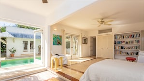 A bedroom with a large bed, a bookshelf, a ceiling fan, and a view of a pool.