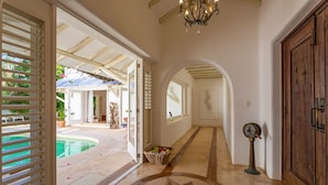 A spacious hallway with a star-patterned floor, a wooden door, and a view of a pool area.