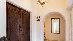 A spacious hallway with a wooden star design on the floor, a chandelier, and a large wooden door.