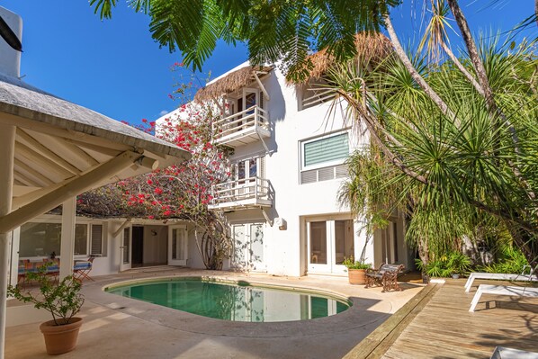 A pool area with a wooden deck, a covered seating area, and a building with a balcony.