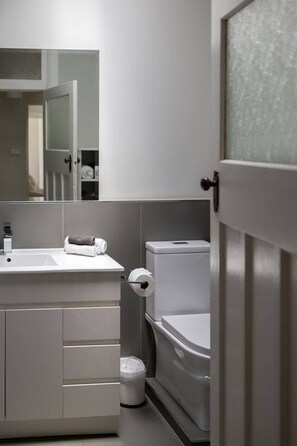 Une salle de bain moderne avec un meuble-lavabo blanc, des toilettes et une poubelle.