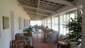 A spacious indoor area with a high ceiling, large windows, and a tiled floor. There are several leather chairs and a sofa arranged along the walls.