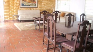 A dining area with a large wooden table and chairs, a sofa, and a painting on the wall.