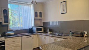 A kitchen with white cabinetry, a granite countertop, a microwave, a toaster, and a window with lace curtains.