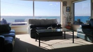 A living room with a view of the sea, a sofa, a coffee table, and a chair.