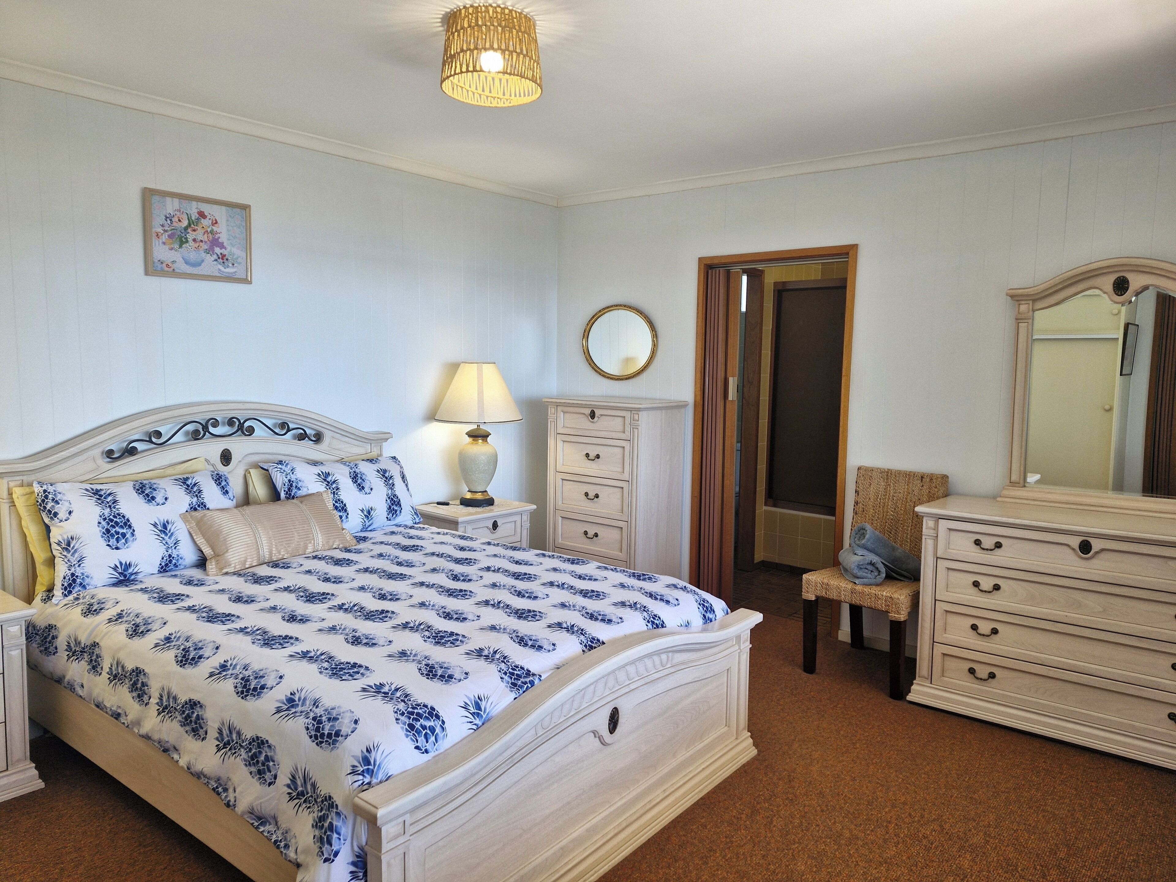 A bedroom with a bed, nightstand, dresser, and a mirror.