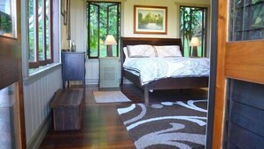 Camera da letto con un letto, lampade sui comodini, una panca in legno e vista sul verde attraverso ampie finestre.