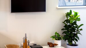 Un saló modern amb televisió de pantalla plana penjada a la paret, un moble blanc d'entreteniment amb una cistella, una planta i una petita escultura de fusta.