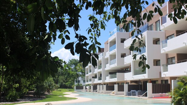Un hôtel moderne doté d’une piscine, entouré d’une végétation luxuriante et surplombant un ciel d’un bleu éclatant.