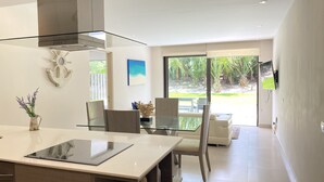 Une cuisine moderne avec une table à manger en verre, une cuisinière intégrée et une vue sur le jardin à travers de grandes fenêtres.