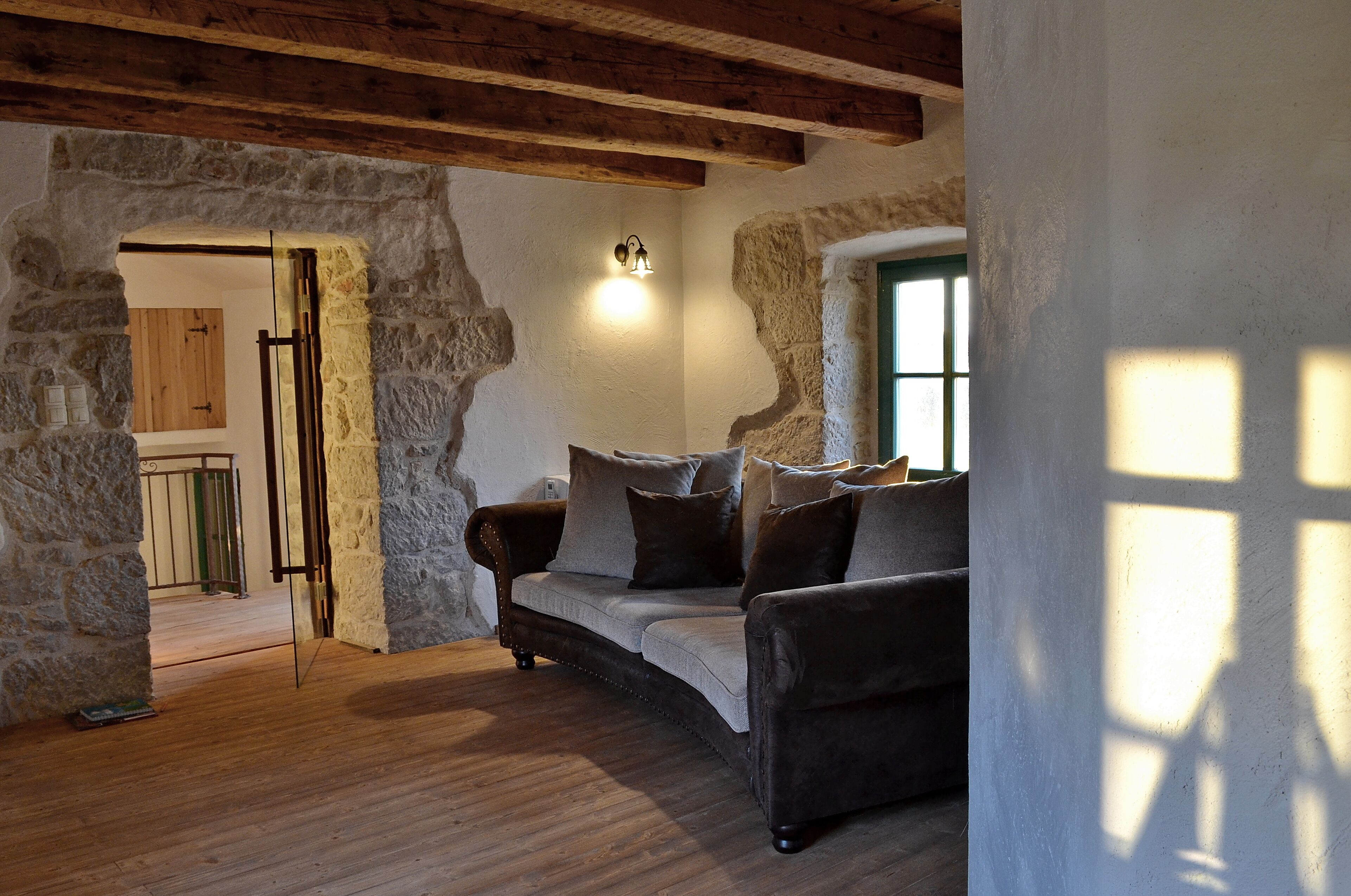 Une pièce rustique aux murs en pierre apparents, au plafond en bois et agrémentée d’un canapé confortable avec des coussins.