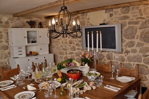 Una mesa de comedor dispuesta con platos, vasos y diversos platillos, rodeada de paredes de piedra y vigas de madera.