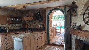 Cocina rústica con armarios de madera, pared de piedra y vista a una piscina a través de un arco.