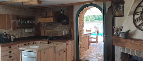 Cocina rústica con armarios de madera, pared de piedra y vista a una piscina a través de un arco.
