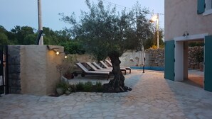 Un patio empedrado con sillones de descanso, un árbol y una piscina.