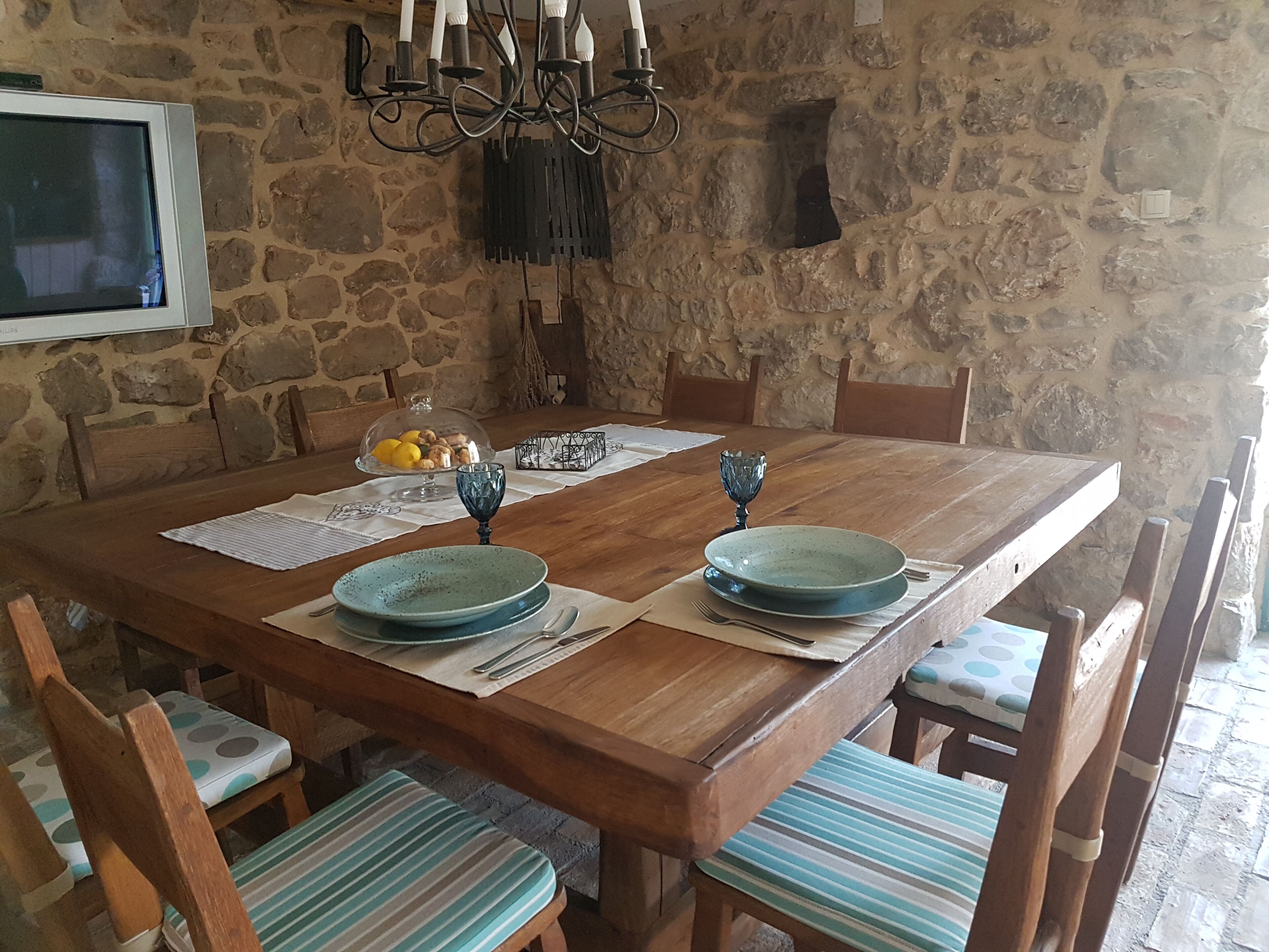 Una mesa de comedor de madera con platos azules, una araña y paredes de piedra.