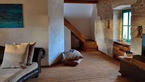 Una habitación rústica con suelo de madera, un sofá con cojines, una escalera y una pared de piedra.