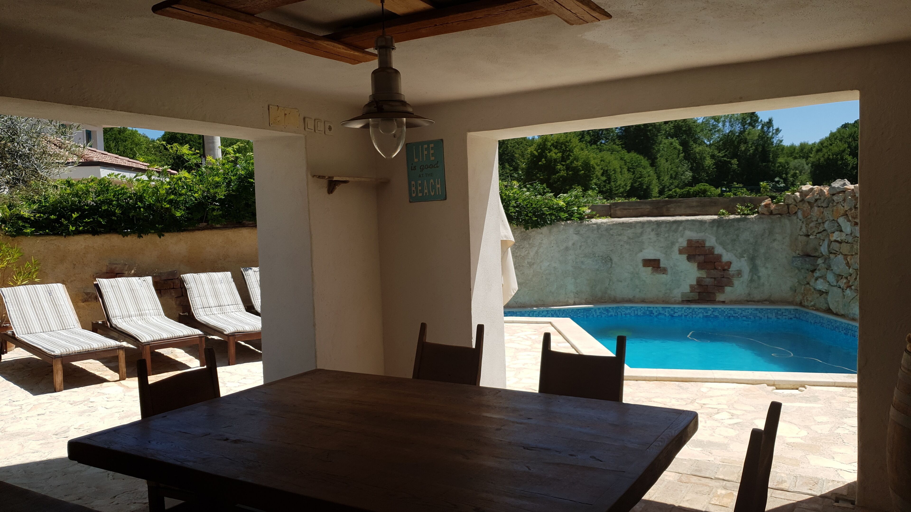 A covered outdoor area with a pool, lounge chairs, and a wooden table.