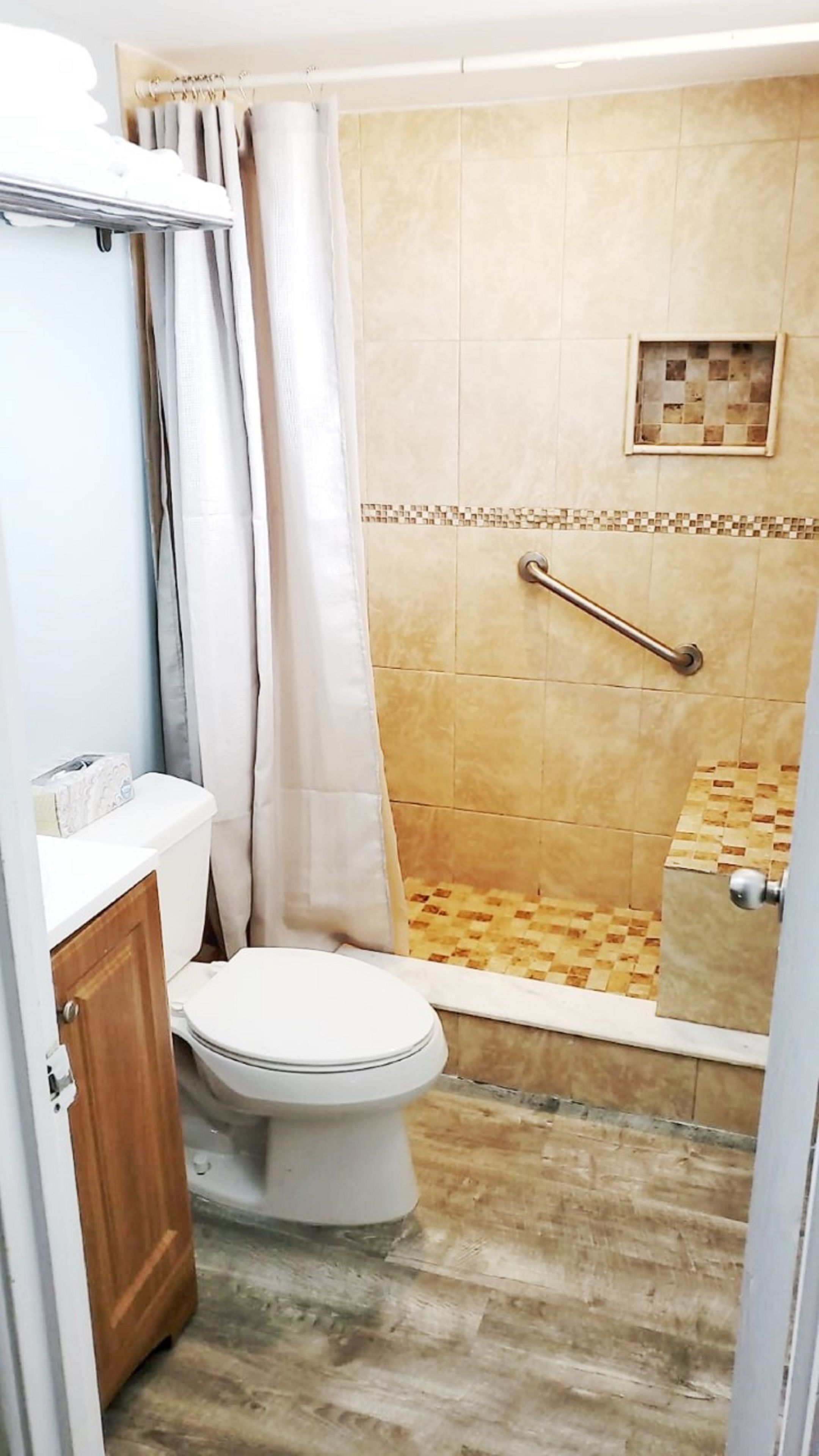 Un baño con ducha, inodoro y un estante pequeño con artículos de aseo.