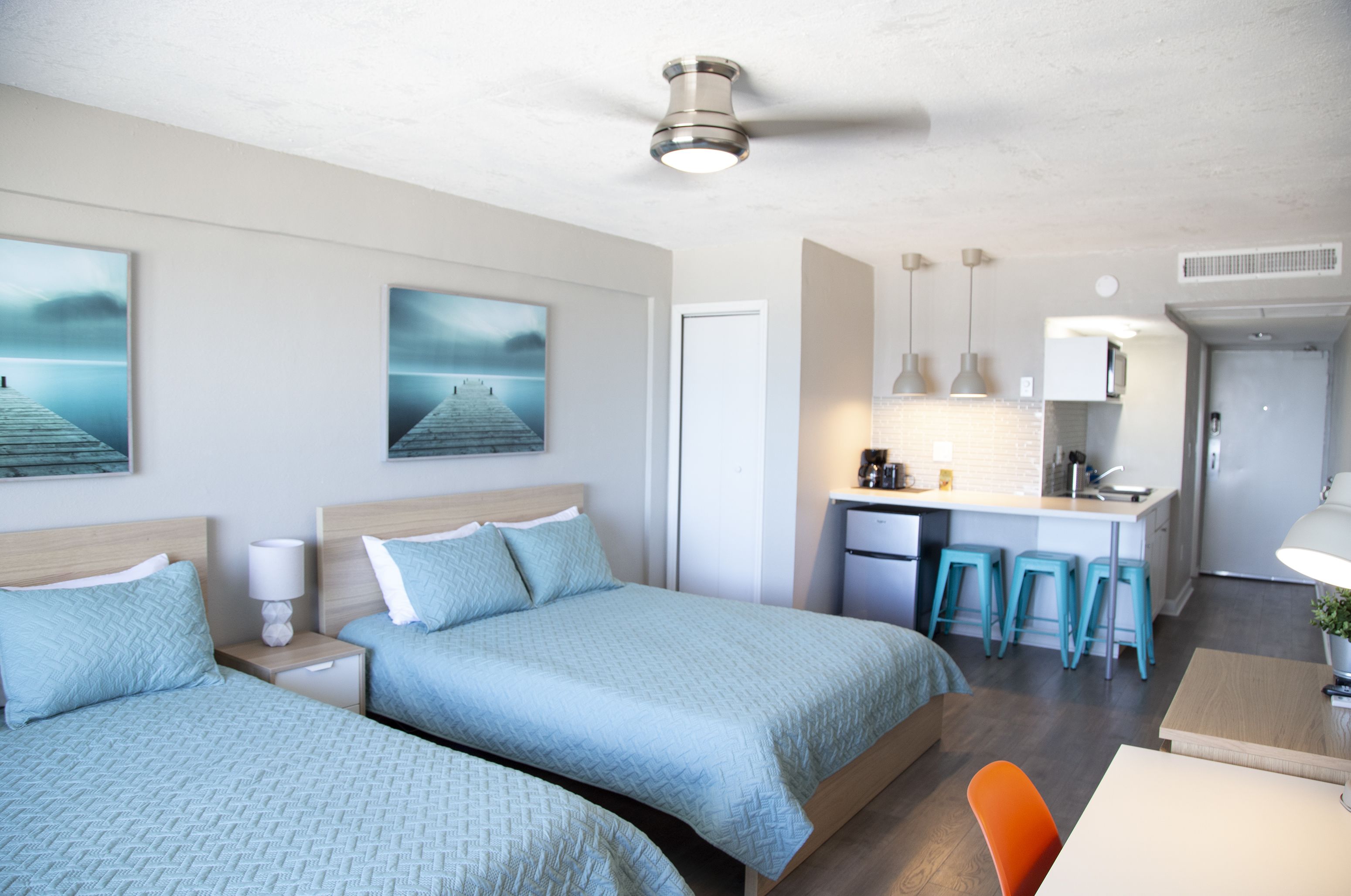Quarto de hotel moderno com duas camas, uma cozinha compacta e área de jantar.