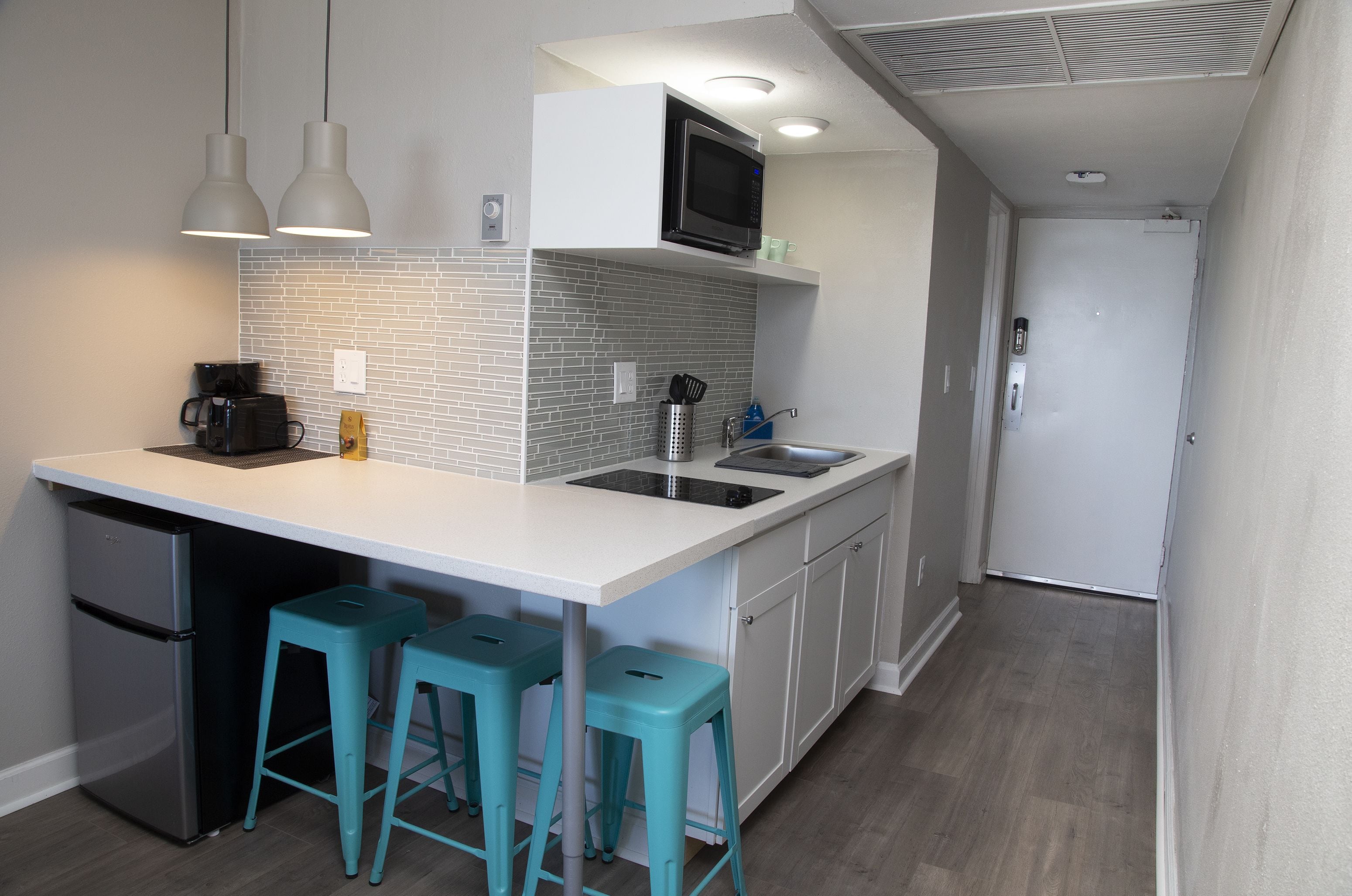 A compact kitchen with a microwave, coffee maker, and bar stools.