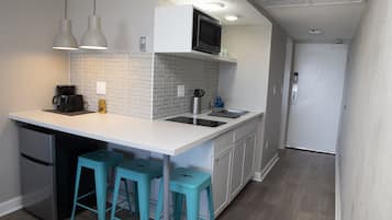 A compact kitchen with a microwave, coffee maker, and bar stools.