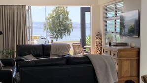 A living room with a black sofa, a wooden cabinet, and a TV on the wall. - Relax, unwind and enjoy the views from this unbeatable lakeside location. (Two Mile Bay (2 Mile Bay))
