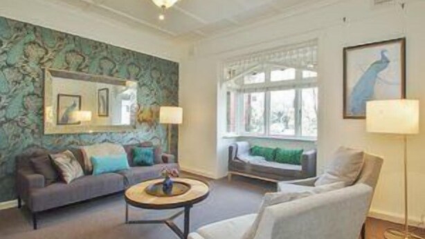 Un salon comprenant un canapé, un fauteuil et une table basse, une grande fenêtre avec des rideaux et un mur orné d’un motif décoratif.