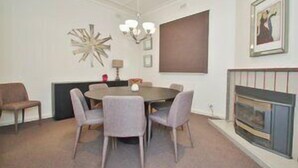 Une salle à manger avec une table ronde et six chaises, un lustre, une cheminée et un tableau encadré au mur.