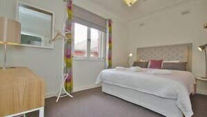 Une chambre à coucher comprenant un lit, une table de chevet, un miroir, une fenêtre avec des rideaux et un luminaire au plafond.