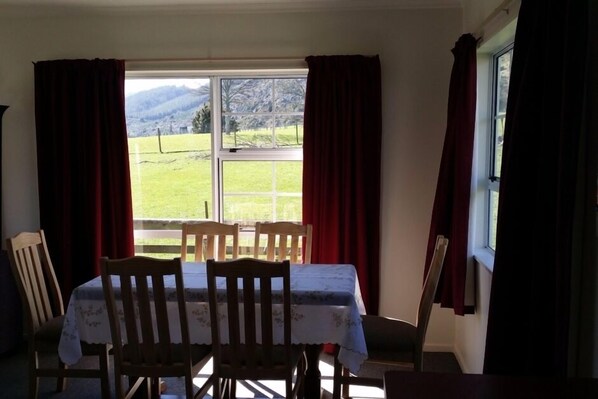 A dining area with a table and chairs, a window with curtains, and a view of a grassy field.
