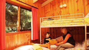 Une chambre dans un chalet en bois, avec des lits superposés, une fenêtre avec des rideaux et une vue sur les arbres.