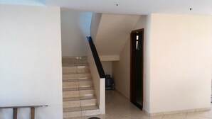 Una escalera con baldosas color beige que lleva a un rellano, una barandilla negra y una puerta a la derecha.