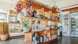 Een winkel met houten planken vol met diverse producten, een koelkast en potplanten.