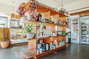 Een winkel met houten planken vol met diverse producten, een koelkast en potplanten.