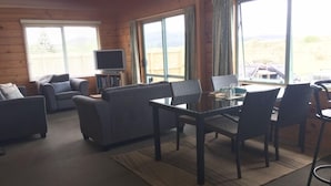 A cozy living room with a sofa, armchairs, a coffee table, and a TV. Large windows offer a view of the outdoors. - Seabed Bach Tokerau Beach (Karikari Peninsula)