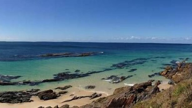 Un paysage côtier caractérisé par une eau turquoise et limpide, des affleurements rocheux et des plages de sable.
