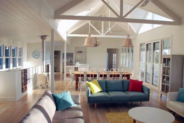 A spacious living area with a high ceiling, a dining table, and a sofa with cushions.