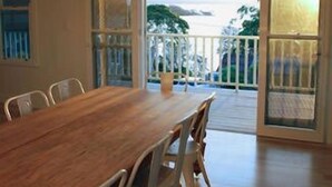 Un espace repas avec une longue table en bois et des chaises en métal, de grandes fenêtres et une vue sur l’extérieur.