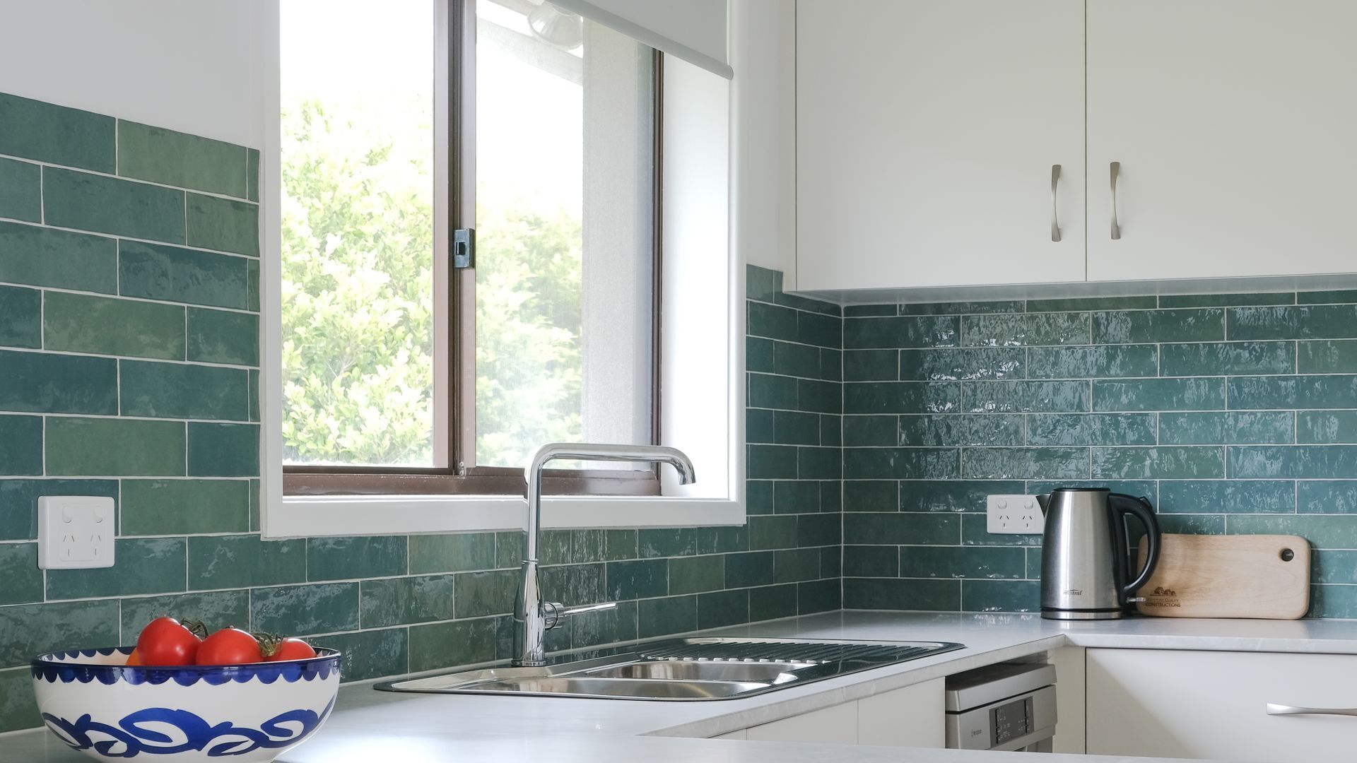Eine moderne Küche mit grünen Fliesen, einem Fenster, einer Spüle und einem Wasserkocher.