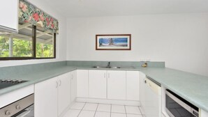 A kitchen with white cabinets, a green countertop, a sink, and a window with a floral curtain.